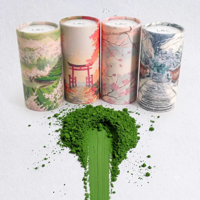 Four hand-illustrated Lạc canisters with a scoop of vivid green matcha powder spilled in front