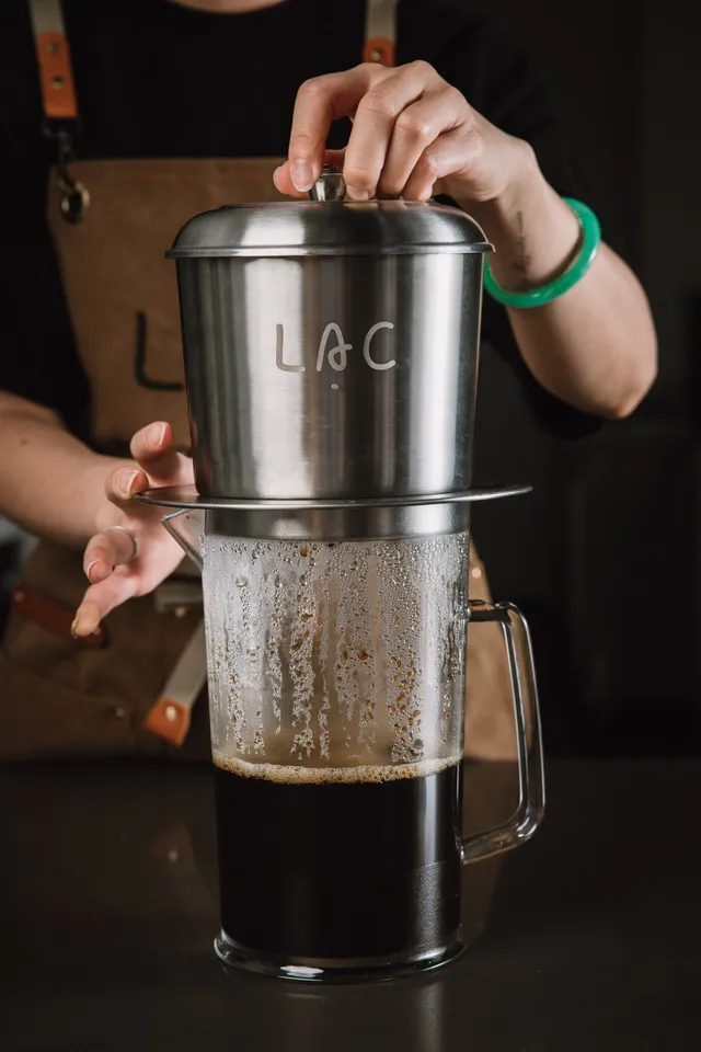 Barista lifting a Lạc Coffee phin filter off a pitcher of freshly dripped Vietnamese coffee