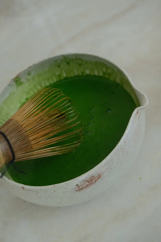 Bamboo whisk resting in a bowl of hand-whisked matcha, LAC stamped into the rim
