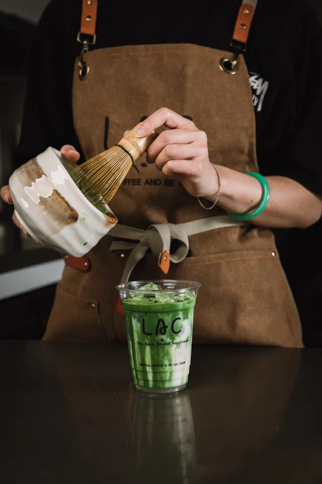 Barista whisking ceremonial matcha with a chasen beside an iced matcha latte