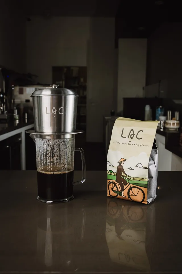 Phin filter dripping Vietnamese coffee into a pitcher beside a bag of Lạc Coffee beans